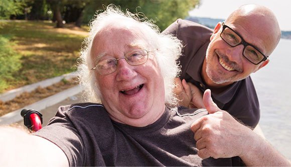 Behinderter Mensch im Rollstuhl, begleitet von einem pers&ouml;nlichen Assistenten. Beide lachen und sind guter Stimmung.